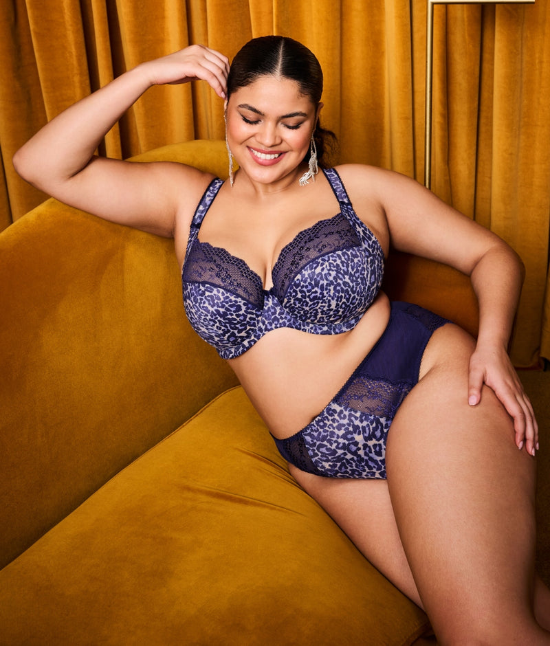 Model wearing Elomi Lucie Plunge Bra and Brief set in Midnight lounging on yellow sofa